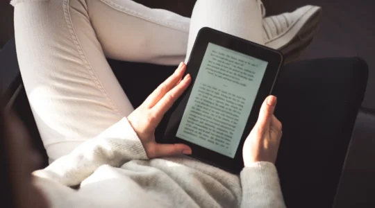 Une femme compare une liseuse et un livre papier dans son salon lumineux.